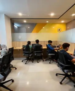 People working in a modern coworking office space with computers and ergonomic chairs.