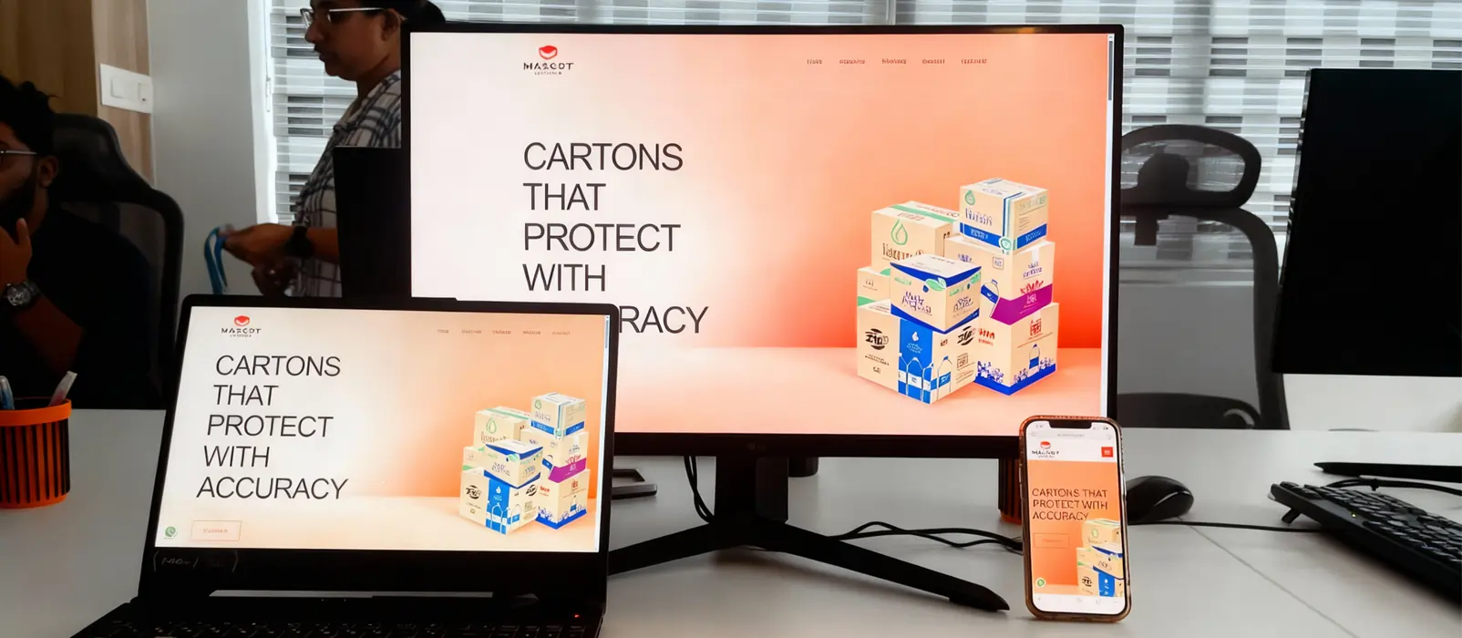 Responsive website UI/UX design displayed on laptop, monitor, and mobile screen in an office setup.